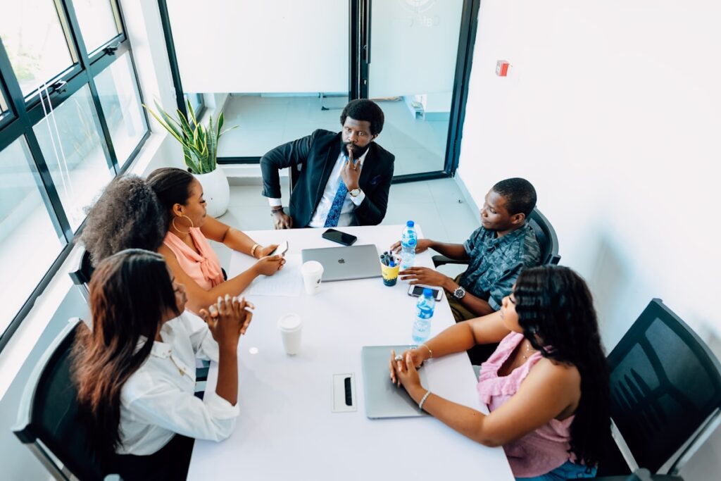 Équipe commerciale de PME B2B en revue de pipeline hebdomadaire autour d'une table de réunion, dirigeant en bout de table animant la discussion