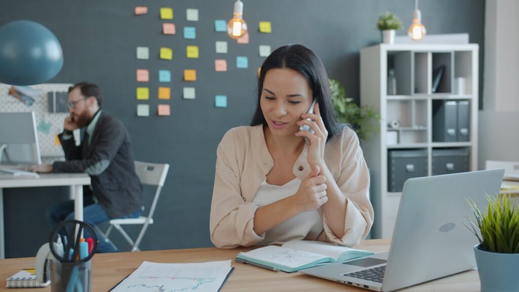 Dirigeante de PME B2B en appel téléphonique professionnel au bureau, ordinateur portable ouvert, scène de prospection commerciale