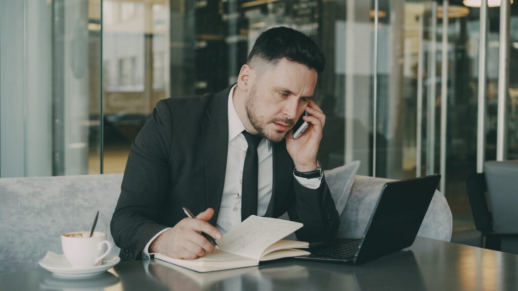 Dirigeant de PME B2B au téléphone qui prend des notes sur un carnet pendant un appel de qualification de cible commerciale
