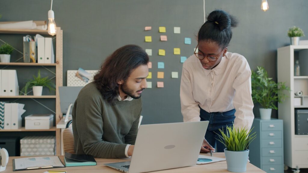Deux collègues d'une PME B2B revoient leur guide de prospection sur un ordinateur portable au bureau
