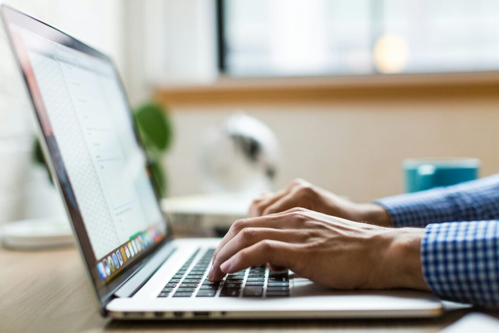 Mains qui tapent sur un MacBook ouvert sur une boite mail dans un bureau lumineux