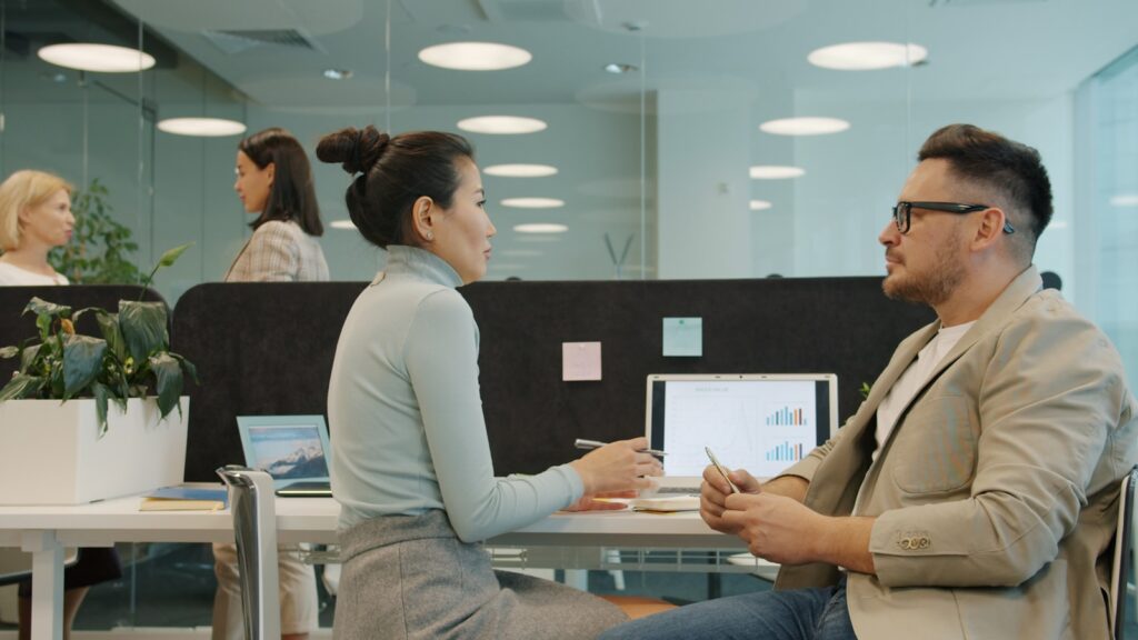 Deux personnes en discussion de débrief commercial autour d'une table dans un bureau moderne après une mission de prospection B2B en PME