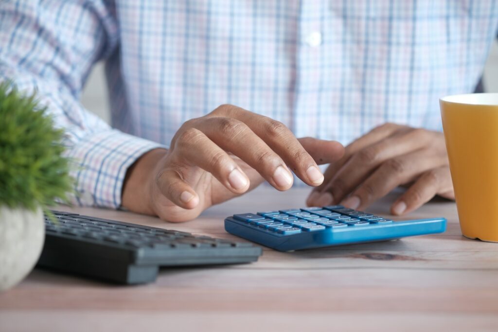 Une main saisit une grille tarifaire B2B sur une calculatrice bleue posée sur un bureau en bois clair