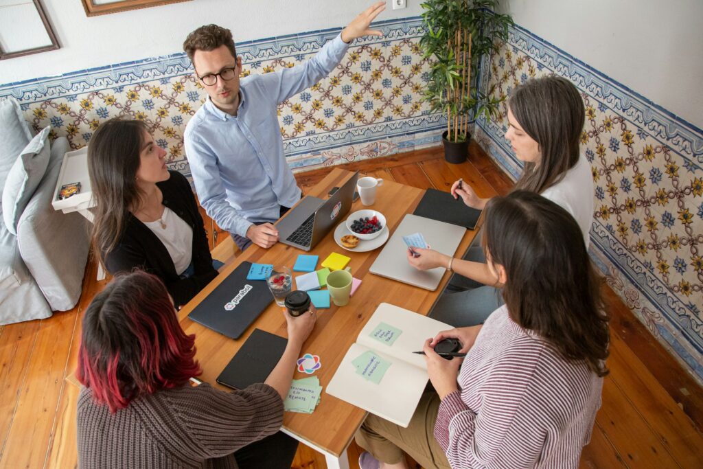 Équipe commerciale de PME B2B en rituel hebdomadaire autour d'une table avec post-its et ordinateur portable
