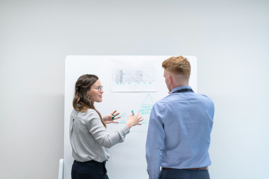 Une manager explique une méthode de prospection à un collègue devant un tableau blanc au bureau