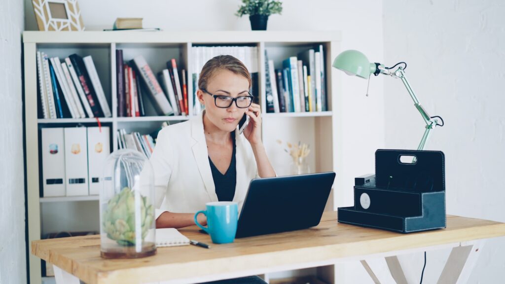 Fondatrice de PME au téléphone à son bureau, concentrée devant son ordinateur portable et son carnet de rendez-vous
