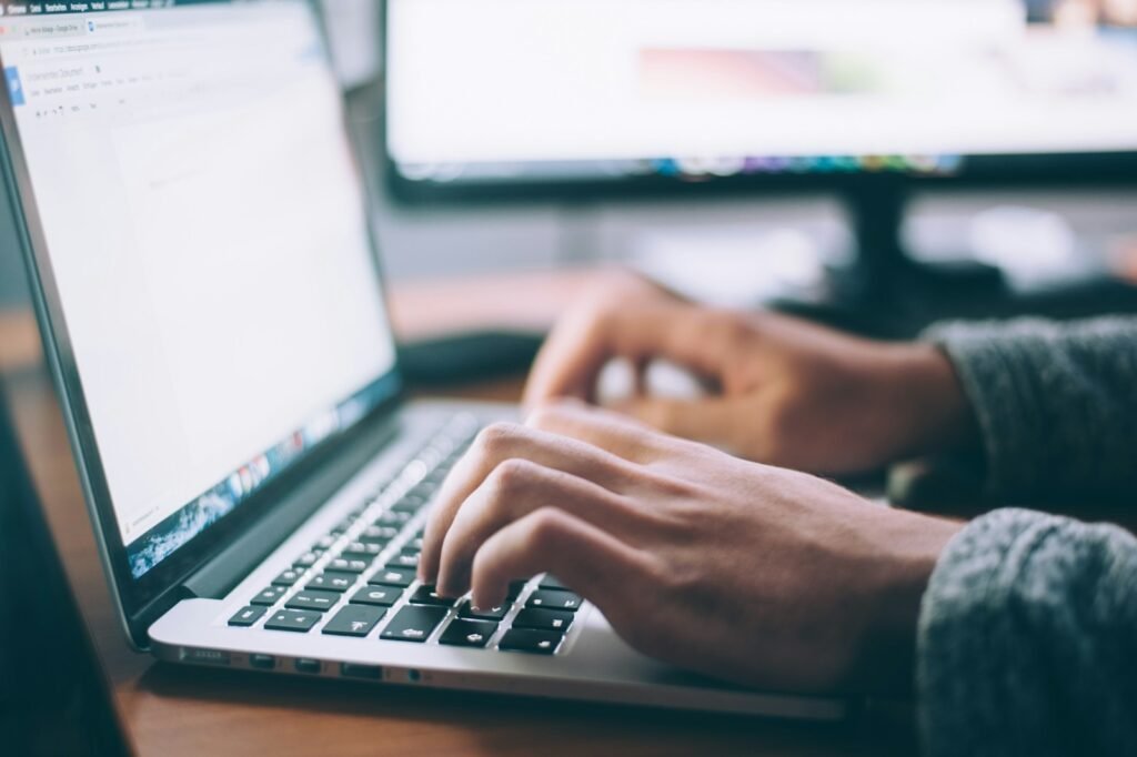 Mains qui tapent sur un ordinateur portable devant un second écran dans un bureau lumineux