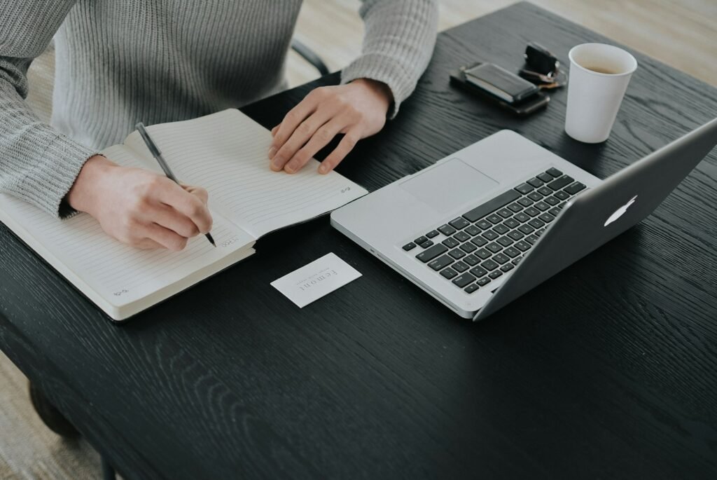 Un dirigeant prépare son plan de prospection dans un carnet à côté de son ordinateur portable