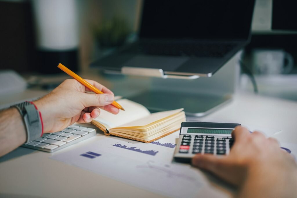 Un dirigeant note ses chiffres dans un carnet, une calculatrice à la main, devant ses graphiques imprimés