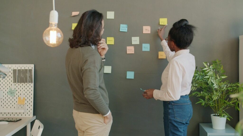 Deux collègues placent des notes adhésives sur un mur pour préparer le plan commercial du trimestre