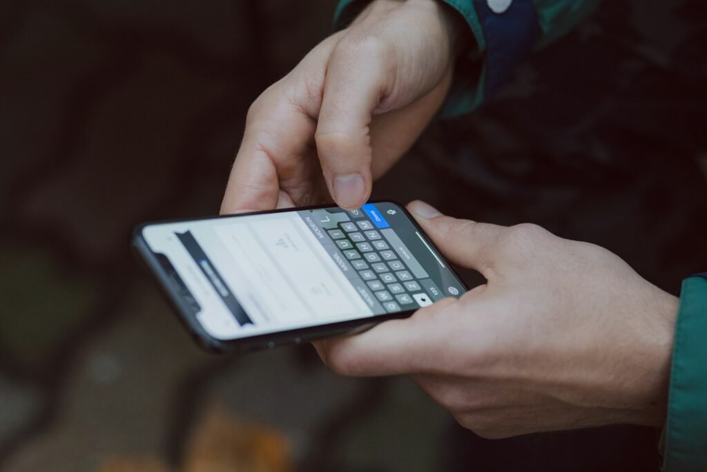 Mains d'une personne qui saisit un texte sur l'écran de son téléphone, en extérieur