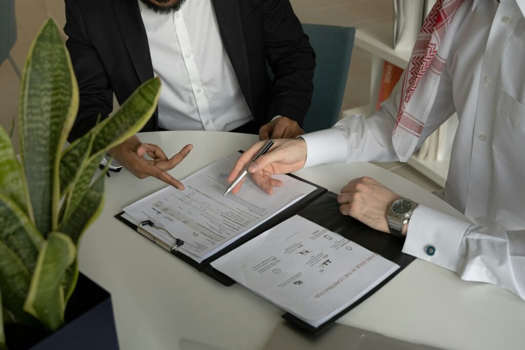 Deux professionnels relisent un dossier client posé sur une table de réunion, stylo pointé sur un chiffre